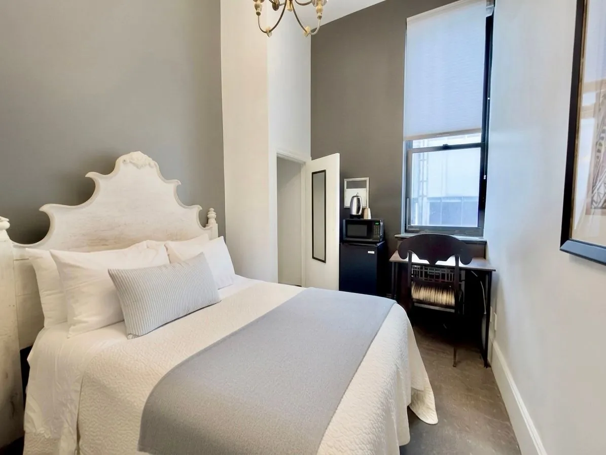 A Deluxe Room with a full bed, upholstered headboard and a desk beside the window