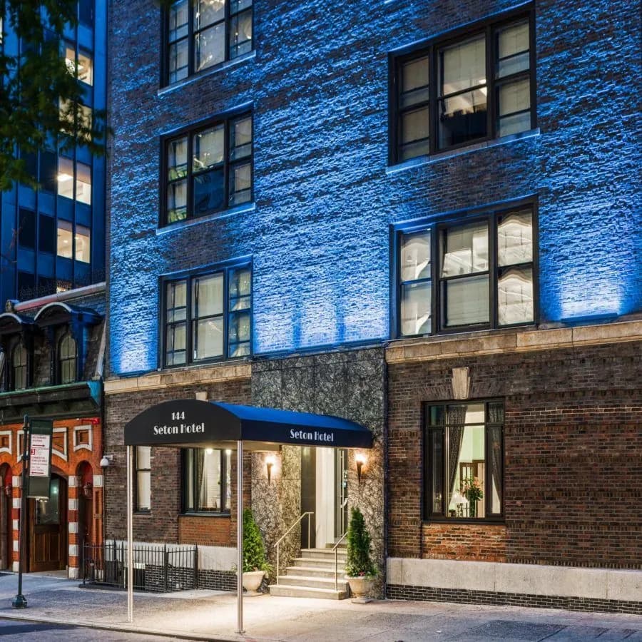 The brick facade of Seton Residence lit blue after dark, with the canopied entrance at street level