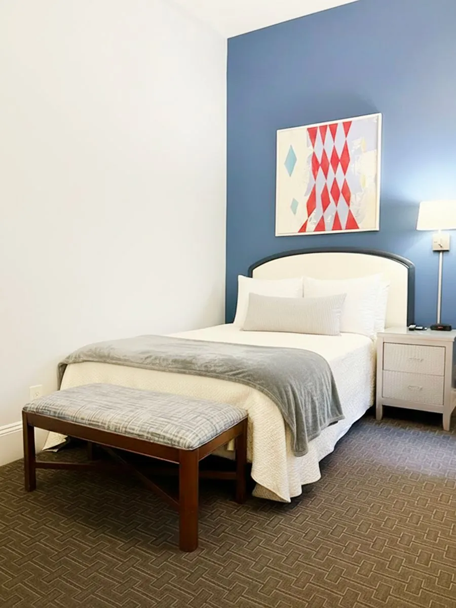 A King Studio with a queen bed against a blue accent wall and a bench at its foot