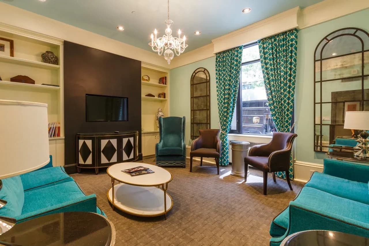 Lounge seating with teal armchairs, a low table and bookshelves either side of the windows